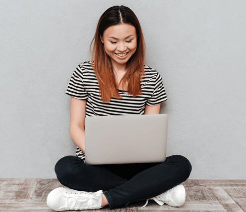 an asian woman sitting on the floor working on her laptop