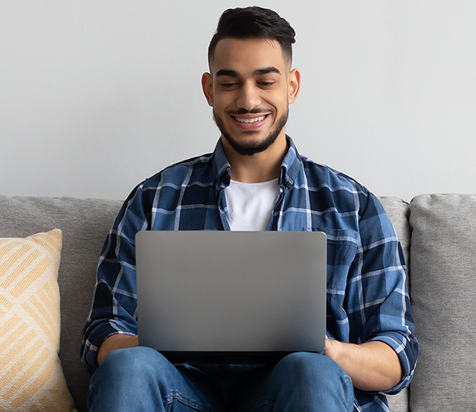 a bearded bald man sitting on a couch working with his laptop